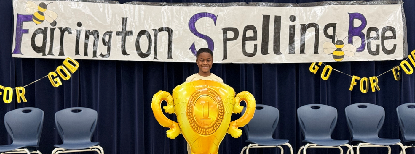 Winner of the Spelling Bee standing behind torphy balloon 